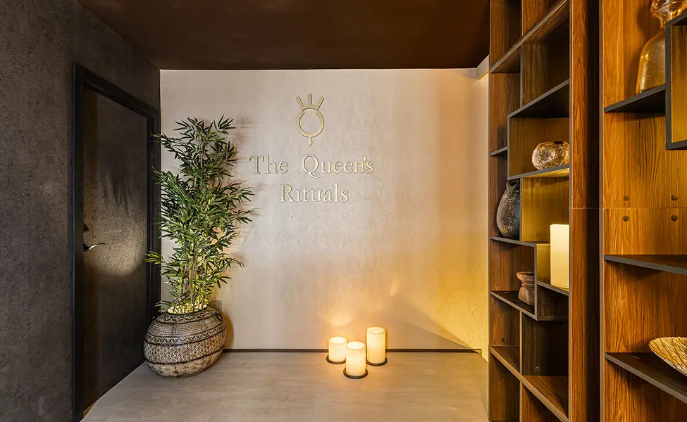 Recibidor de The Queen's Rituals con el logotipo en la pared, velas encendidas y estantería de madera