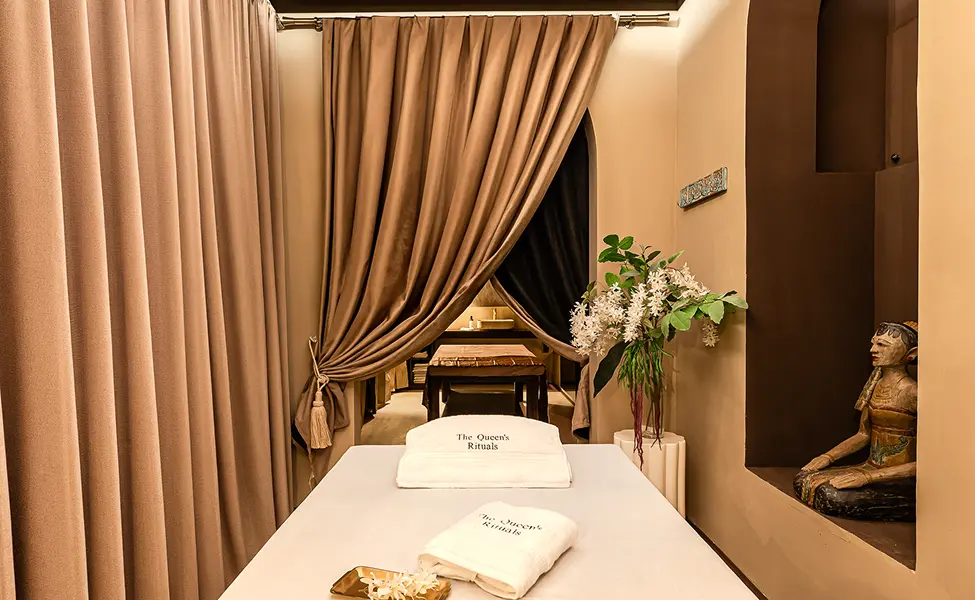 Cabina de masaje de The Queen's Rituals con la camilla preparada, toallas de la casa y cortinas